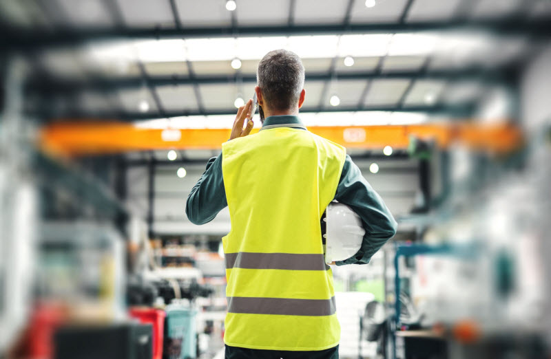 A rear view of an industrial man engineer with smartphone in a factory
