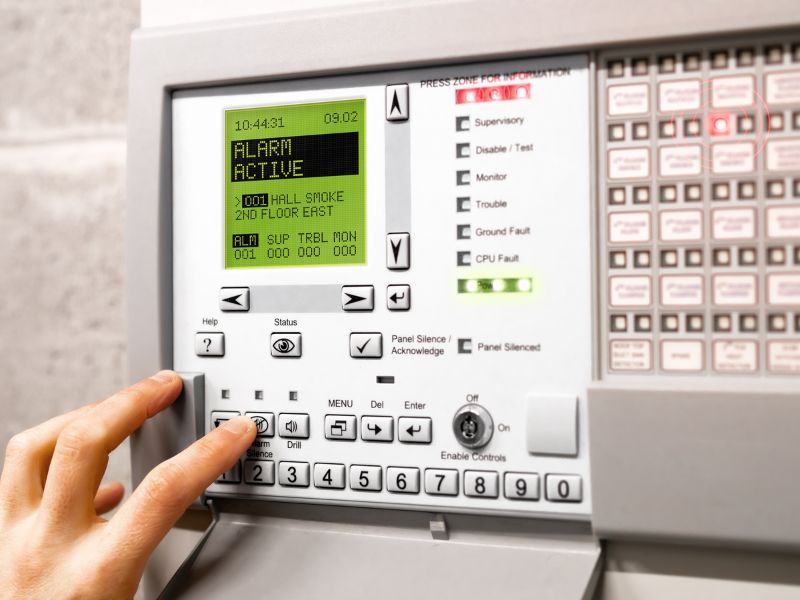 Hand touching button on Fire alarm control panel with Display message: Alarm active hall smoke