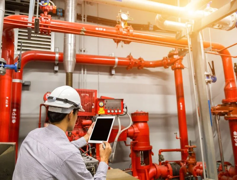 Engineer with tablet check red generator pump for water sprinkler piping and fire alarm control system.